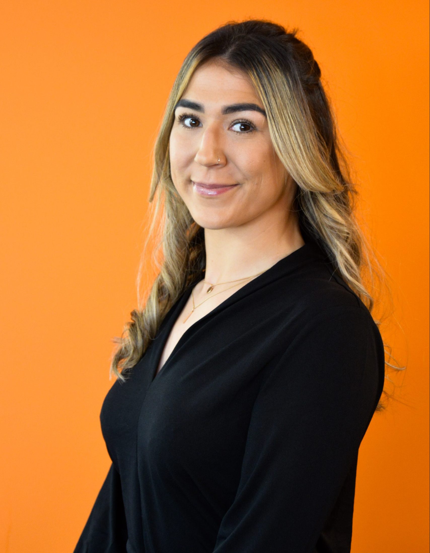 Side on headshot of woman with long, dark blonde hair in front of an orange background